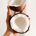 Hand holding 2 halves of coconut with half in their palm and other half in their fingertips